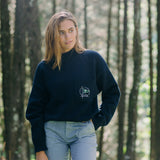 Woman in the woods looks off camera wearing Mariner sweater
