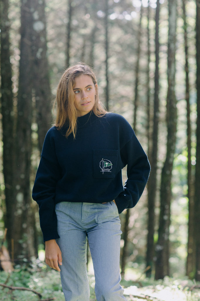 Woman in the woods looks off camera wearing Mariner sweater