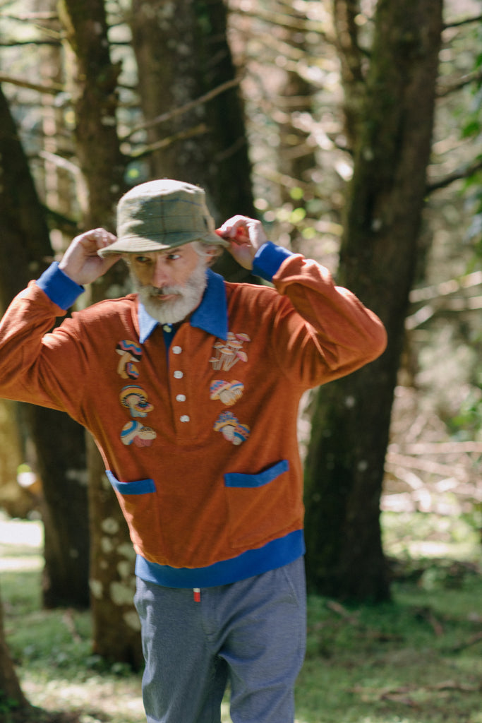 older male model posing in forest in the organic cotton terry cloth long sleeve polo cabana shirt for your new softest sweater that is smart and fun with embroidered mushrooms 