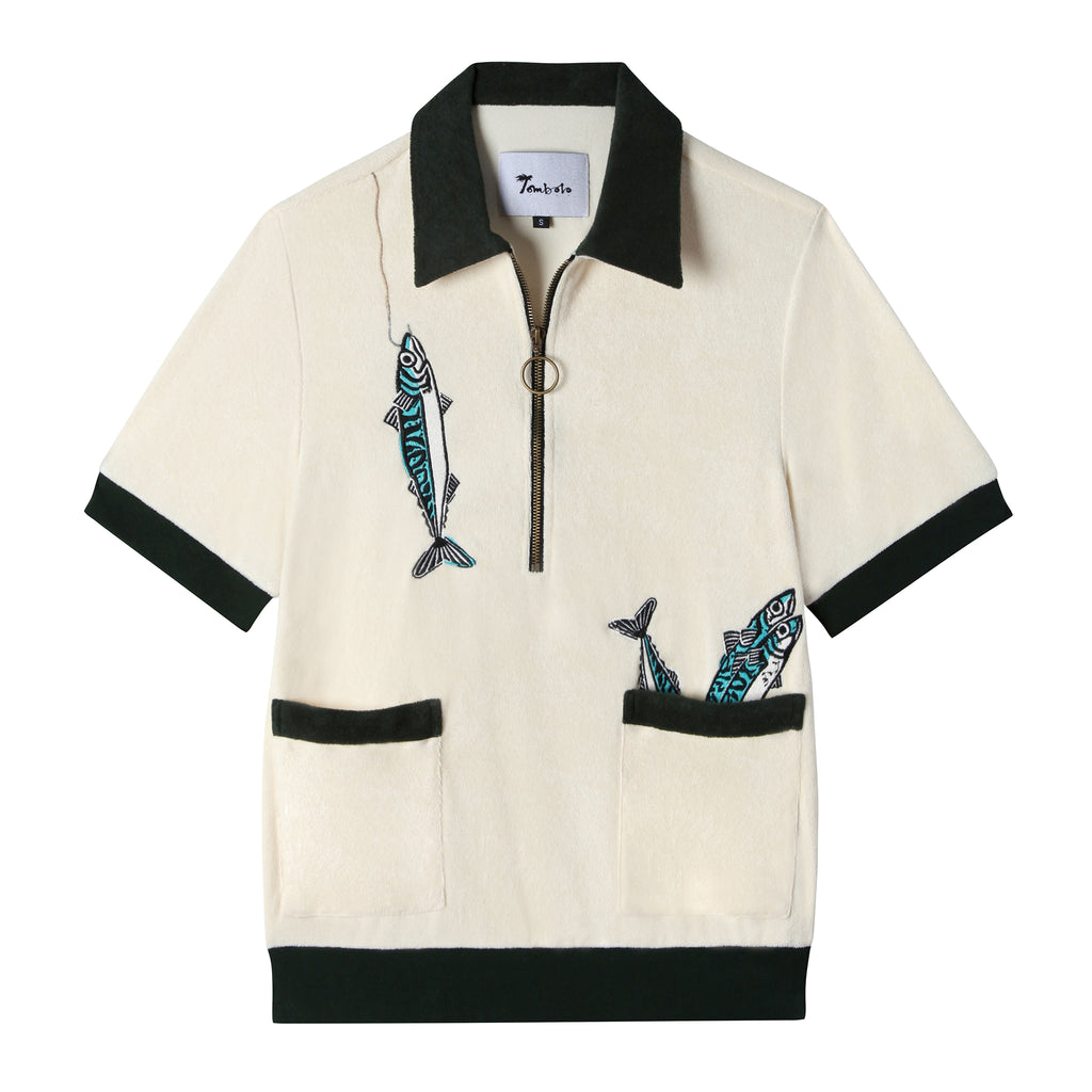 Front view of our Angler Cabana Shirt in cream with forest green on the collar, pockets, and bottom waistband, embroidered with a fish and a hook on the top left and two fish coming out of the bottom right pocket as well as featuring an antique brass half zip
