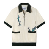 Front view of our Angler Cabana Shirt in cream with forest green on the collar, pockets, and bottom waistband, embroidered with a fish and a hook on the top left and two fish coming out of the bottom right pocket