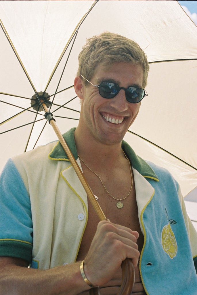 Male model wearing shirt unbuttoned smiling while holding a parasol