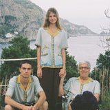Paolo Sandulli outdoors sitting alongside a male and female model, all three wearing the shirt