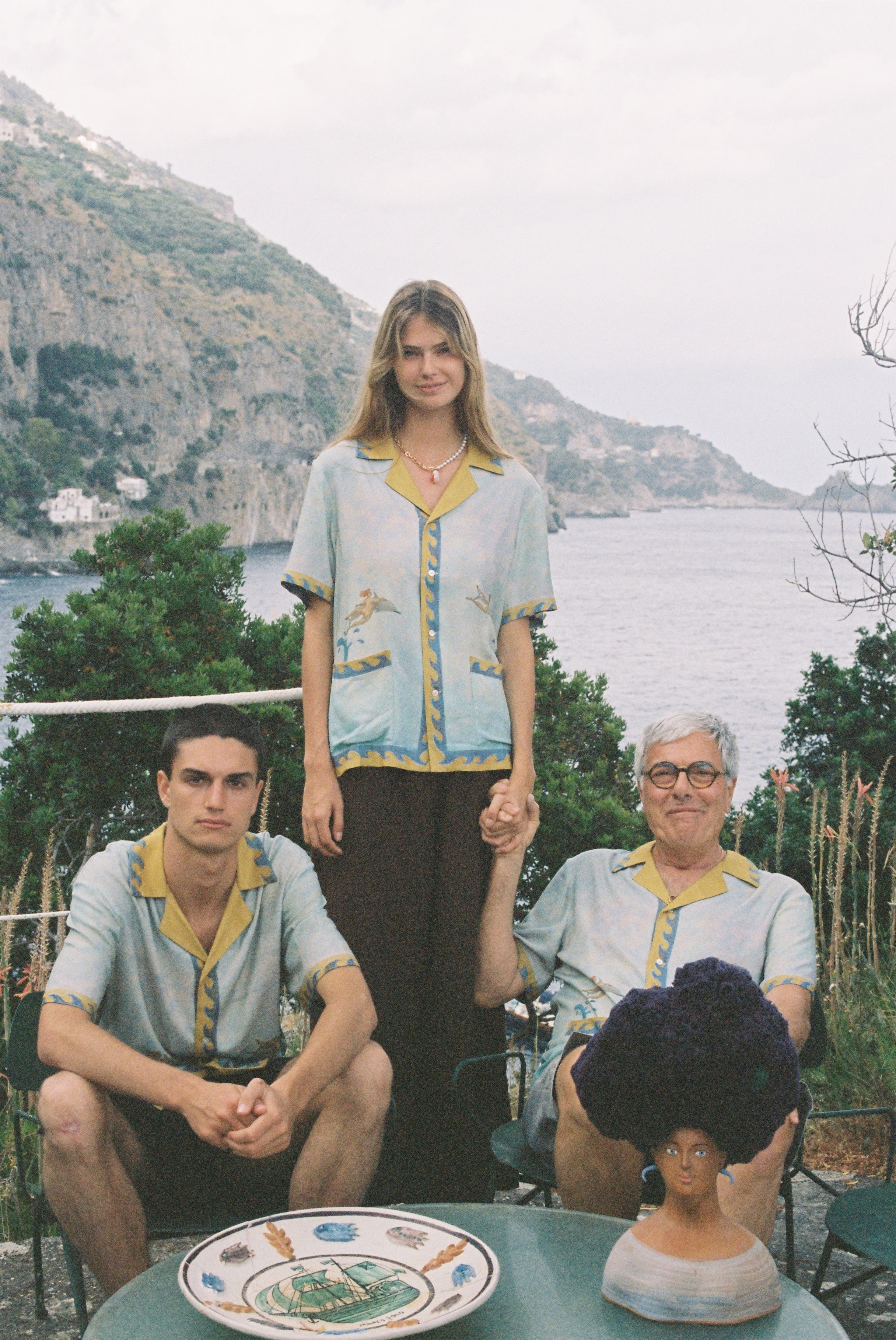 Paolo Sandulli outdoors sitting alongside a male and female model, all three wearing the shirt