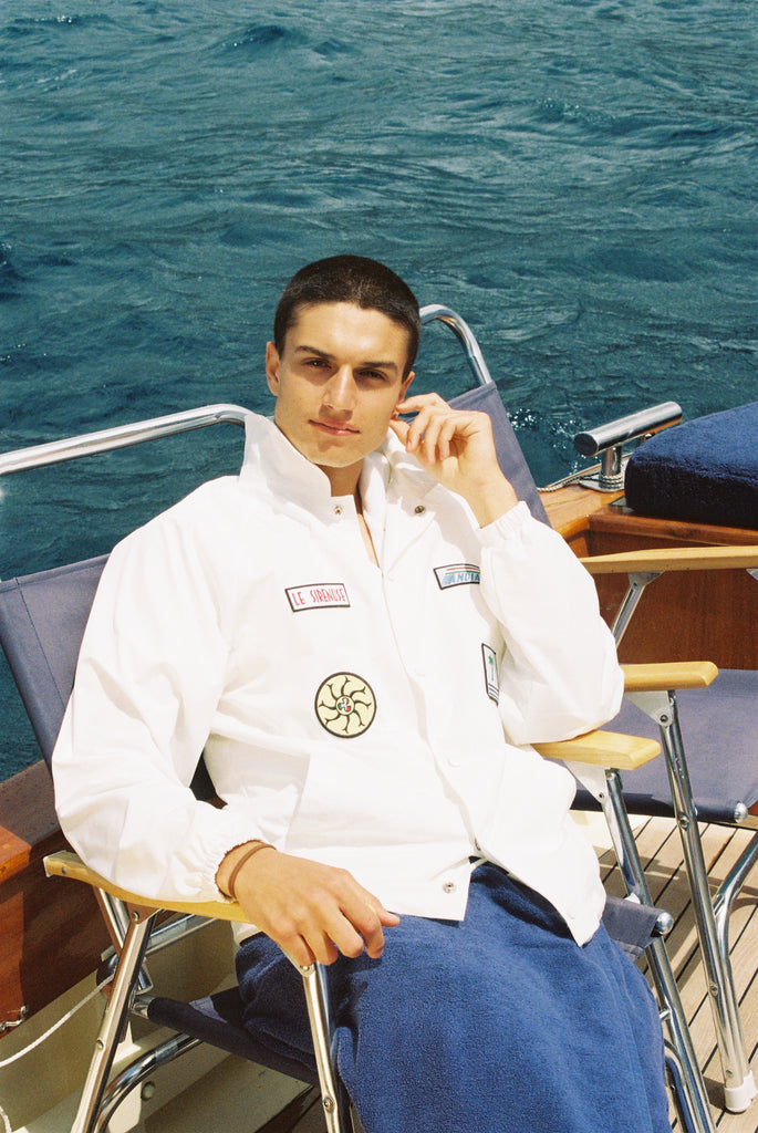 Male model wearing jacket buttoned up sitting down on a boat deck