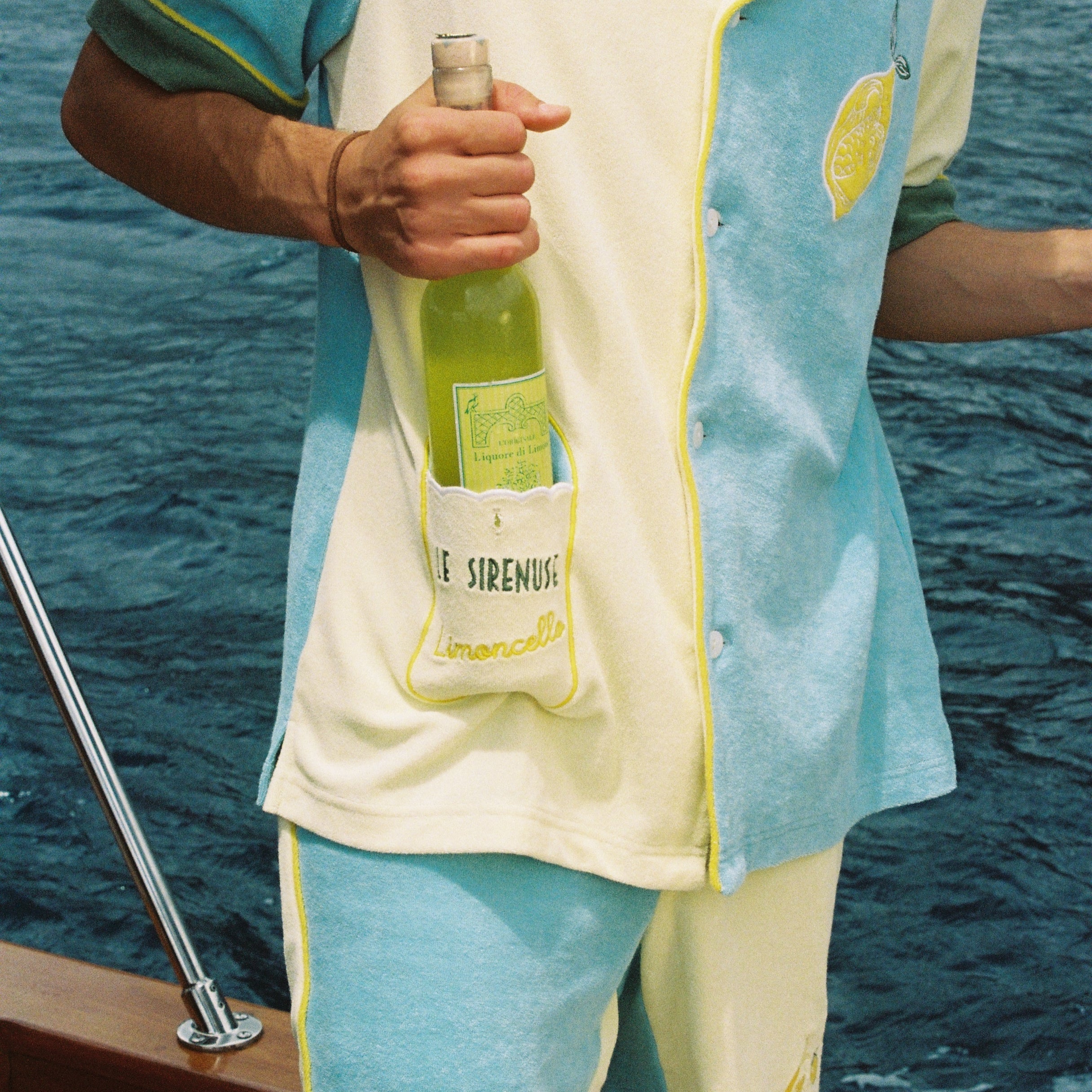 Male model wearing full Limoncello set with shorts on a boat placing a wine bottle inside the limoncello pocket