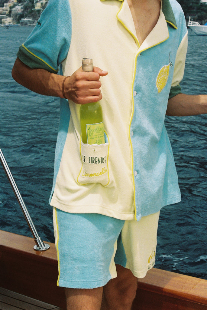 Male model wearing full Limoncello set with shorts on a boat placing a wine bottle inside the limoncello pocket