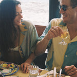 A male and female model dine together while he dons the limoncello shirt and she wears the paolo sandulli collab