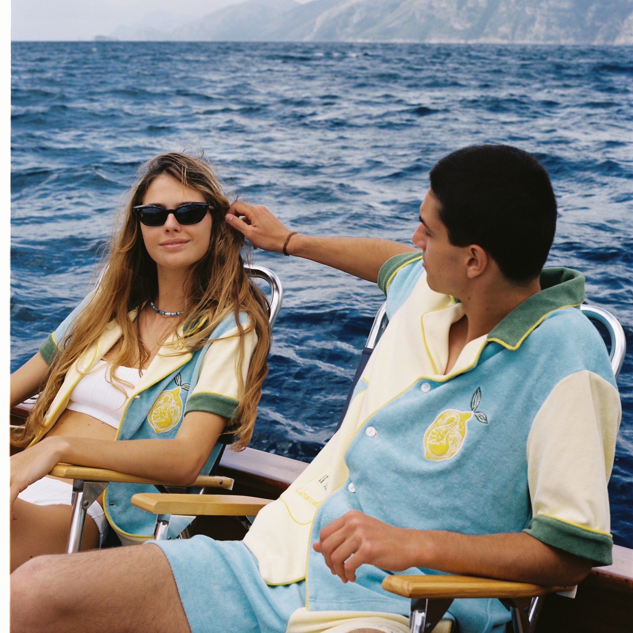 Male and female models wearing the limoncello set lounging in chairs on a boat