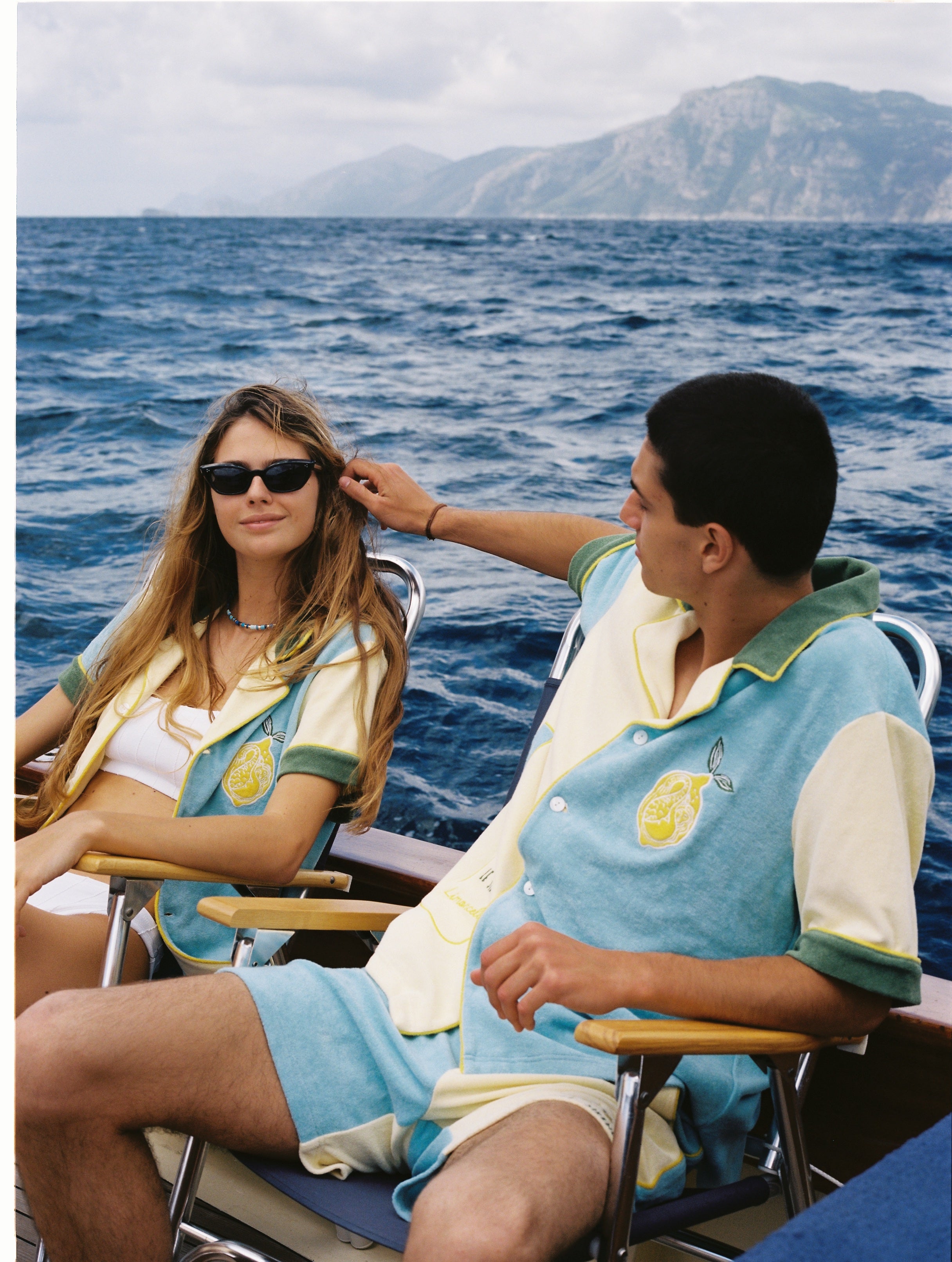 Male and female models wearing the limoncello set lounging in chairs on a boat