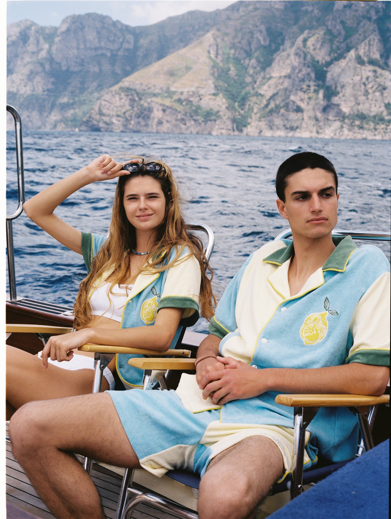 Male and female models sit in chairs on boat donning the limoncello set
