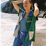 Female model wearing full water sport set over a one piece blue swimsuit with hands in her hair