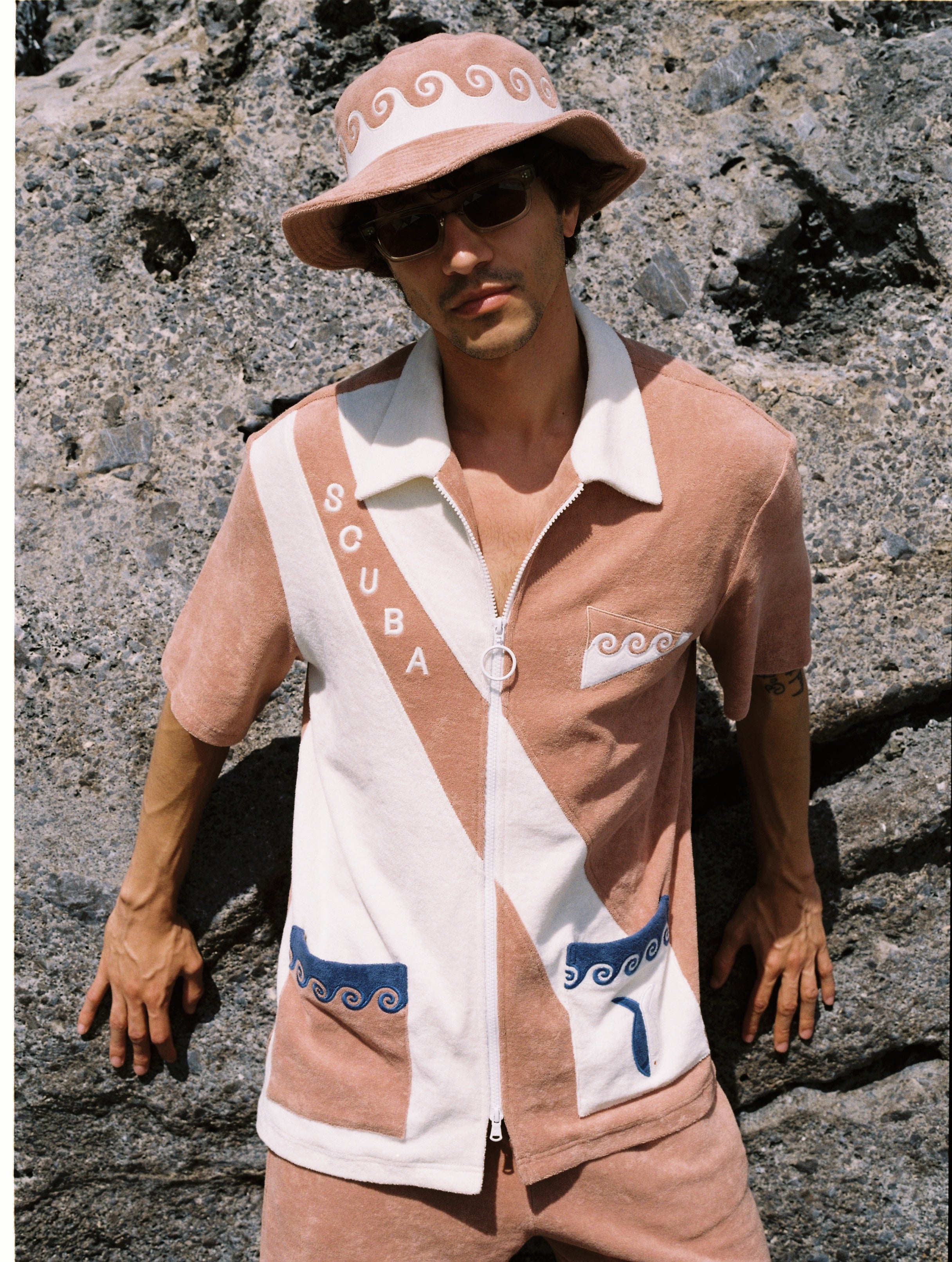male model wearing full set leaning against a beachy rock