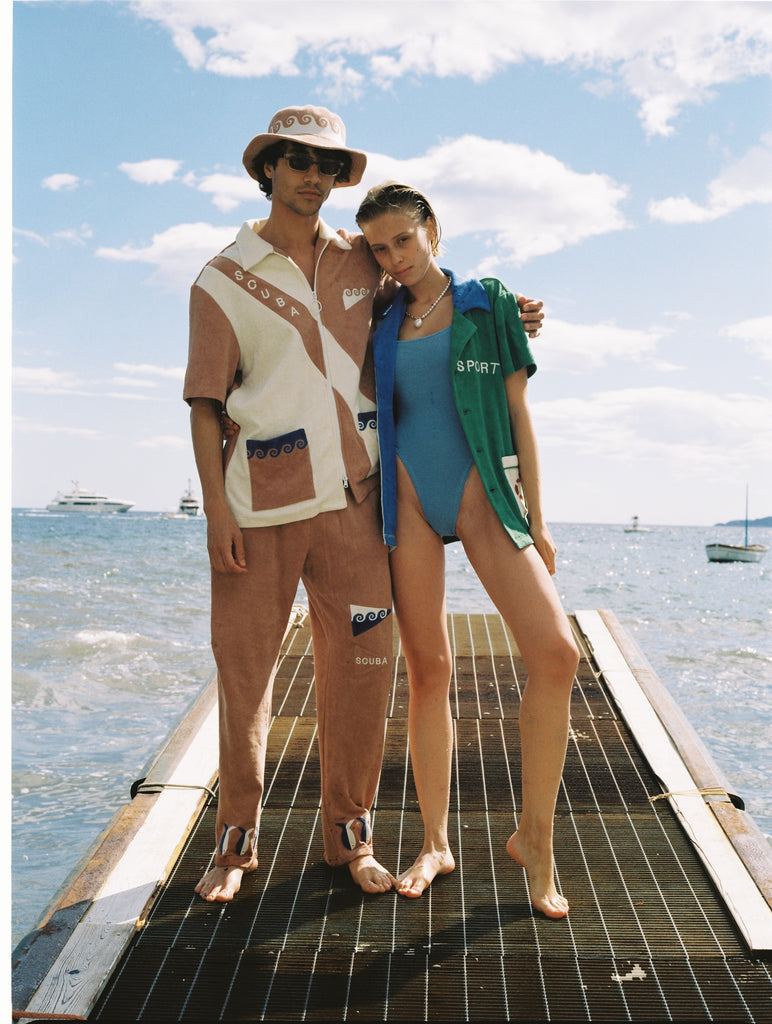 Male model wearing full set with arm around female model wearing water sport cabana