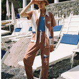 Female model posing in full set on rocky beach with left hand grabbing bucket hat 
