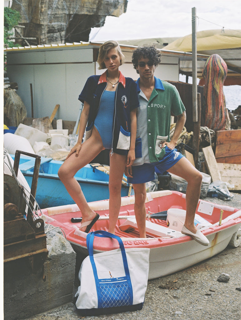 male and female models posing in boat with tote bag leaning against boat on sandy ground