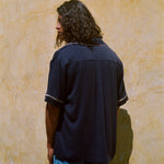 Male model facing a wall showing the back of the shirt with blue jeans 