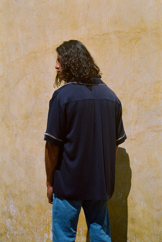 Male model facing a wall showing the back of the shirt with blue jeans 