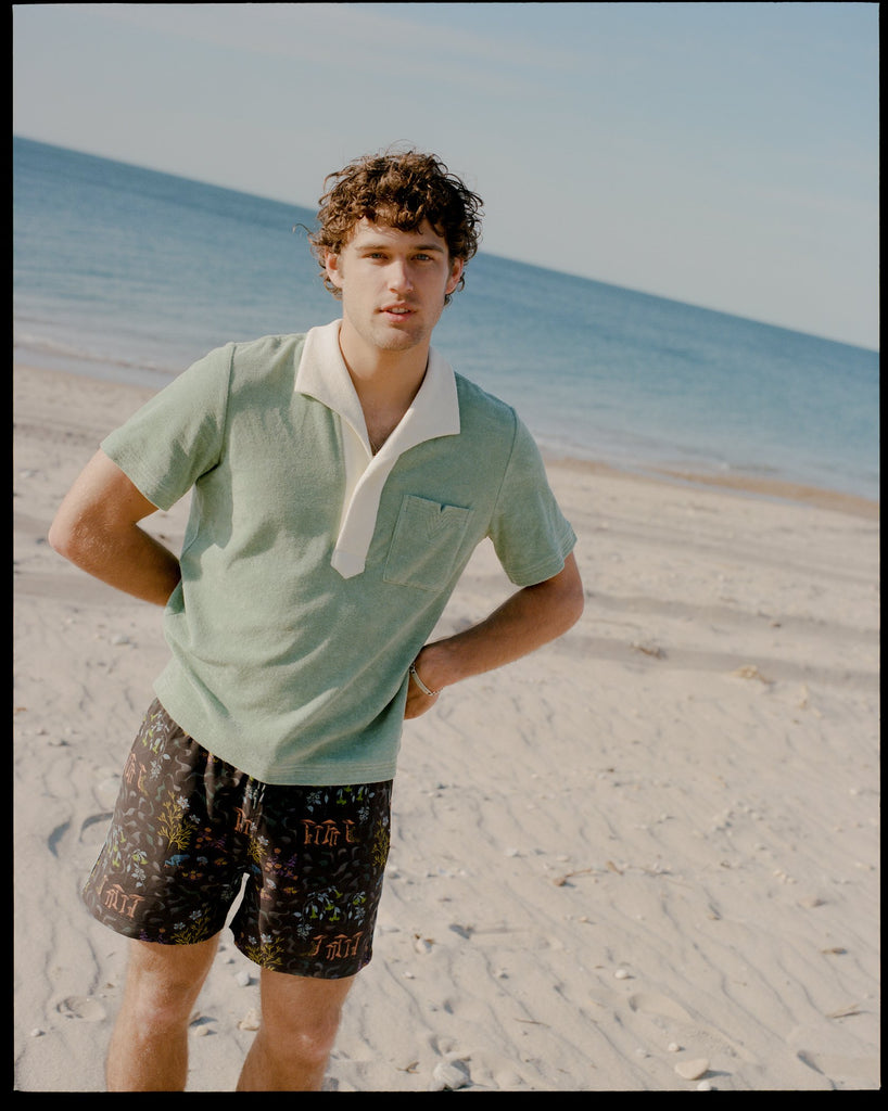 Man stares at camera with hands behind his back in green polo