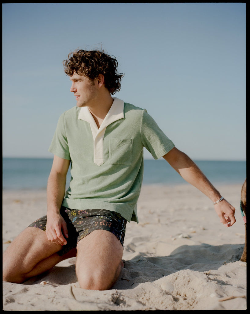 Man kneels on the sand with ocean in background
