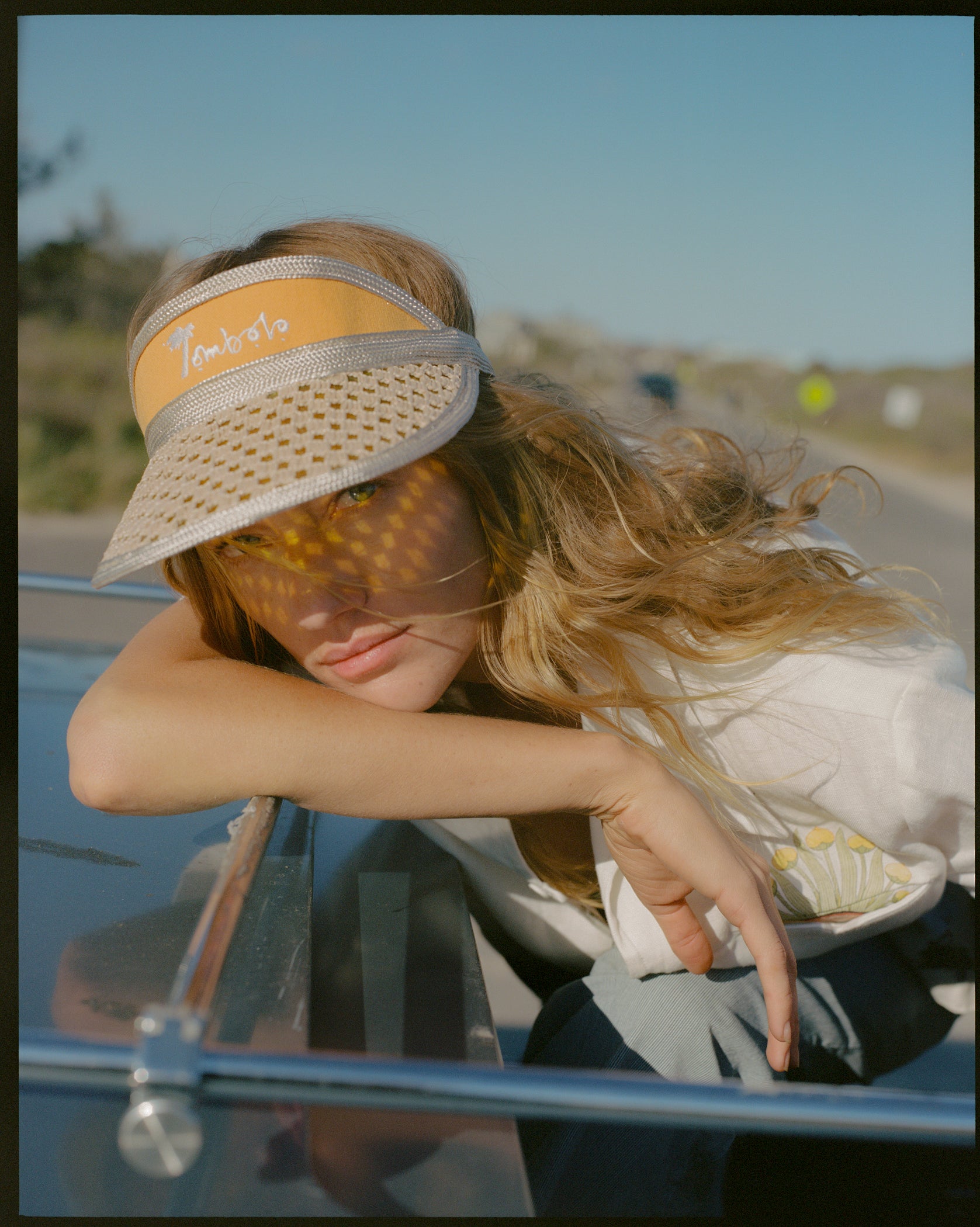 Female model leaning out of car roof wearing visor