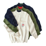 Three different colorways of sweater in navy, cream and green lay on top of eachother