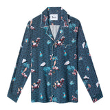 Front lay flat view of shirt with recurring pink Adam and Eve in a tropical garden of Eden print over blue waves with white piping along pocket and collar