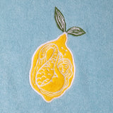 Close up of the white embroidered mermaid inside the lemon on the top right of the shirt