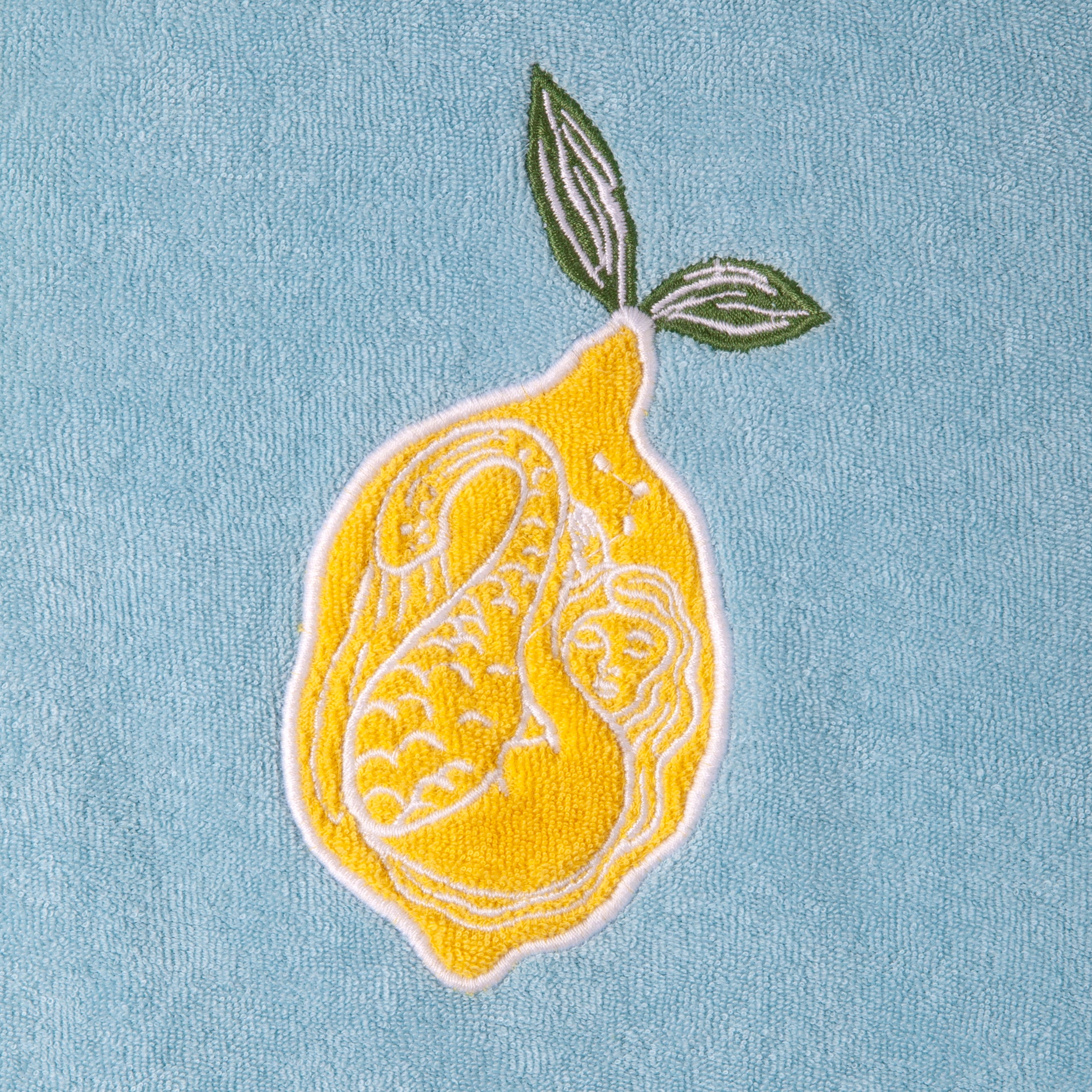 Close up of the white embroidered mermaid inside the lemon on the top right of the shirt