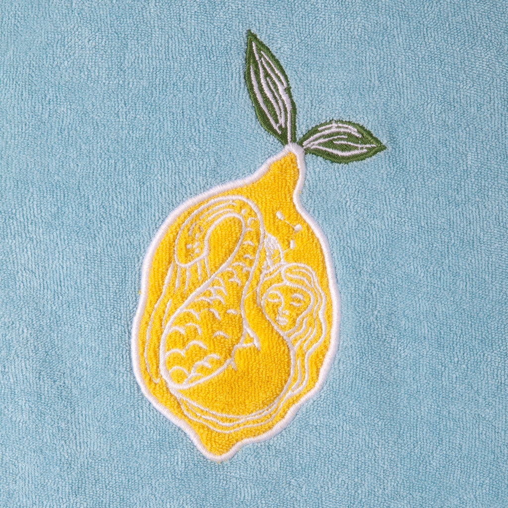 Close up of the white embroidered mermaid inside the lemon on the top right of the shirt