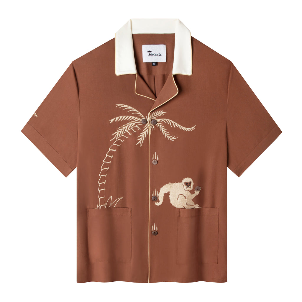 flat lay product photo of our breathable, lightweight Tencel Cabana Shirt featuring a carefully embroidered monkey catching a falling coconut (button) from a palm tree with buttons standing in for coconuts.