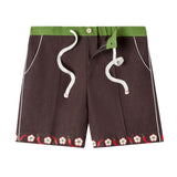 Cabana shorts in brown linen with embroidered red chili peppers and white chili flowers forming a border along both leg openings. Green waistband.  Drawstring untied and zipper undone to show that there is a functional fly.