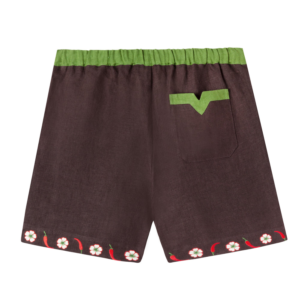 Back view of cabana shorts in brown linen with embroidered red chili peppers and white chili flowers forming a border along both leg openings. Green waistband and one back pocket with v-slit detail.
