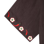 Close up shot of embroidered white flowers and red chili peppers along border of cuff. 