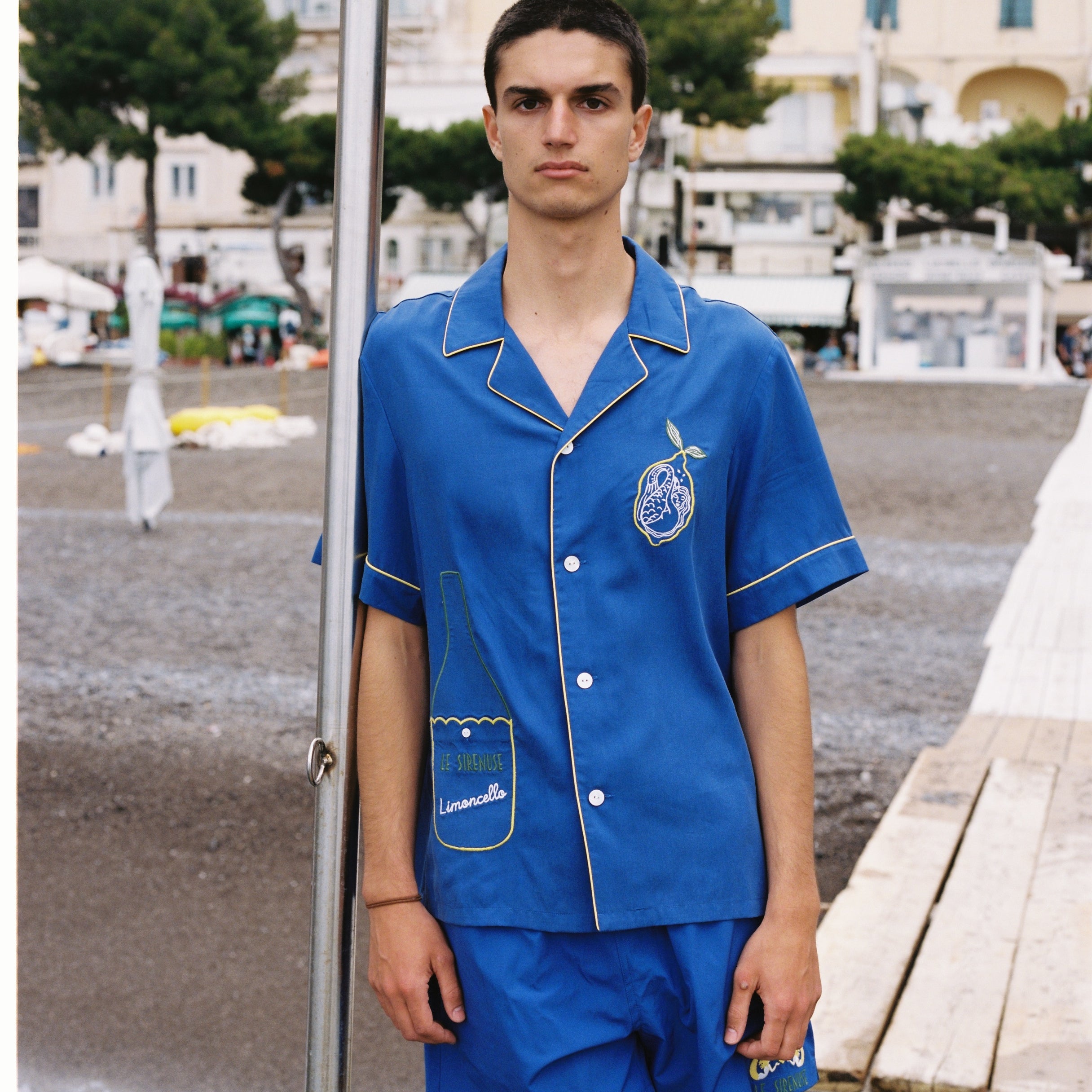 male model in full blue limoncello set leaning against a pole outdoors