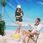 Female model wearing shirt stepping on beach ball while male model sitting down looks on