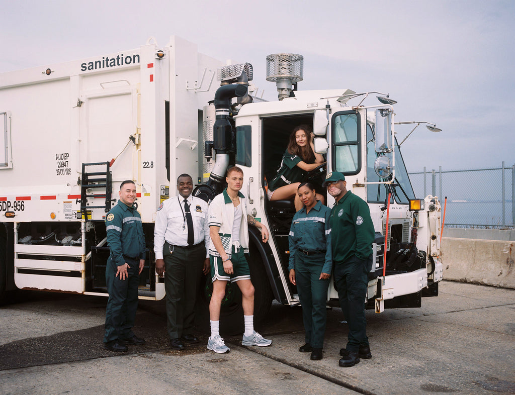 Male model in cabana surrounded by DSNY workers in front of garbage truck