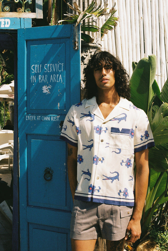 Male model posing in shirt with our Khaki Stowaway shorts next to a beach bar