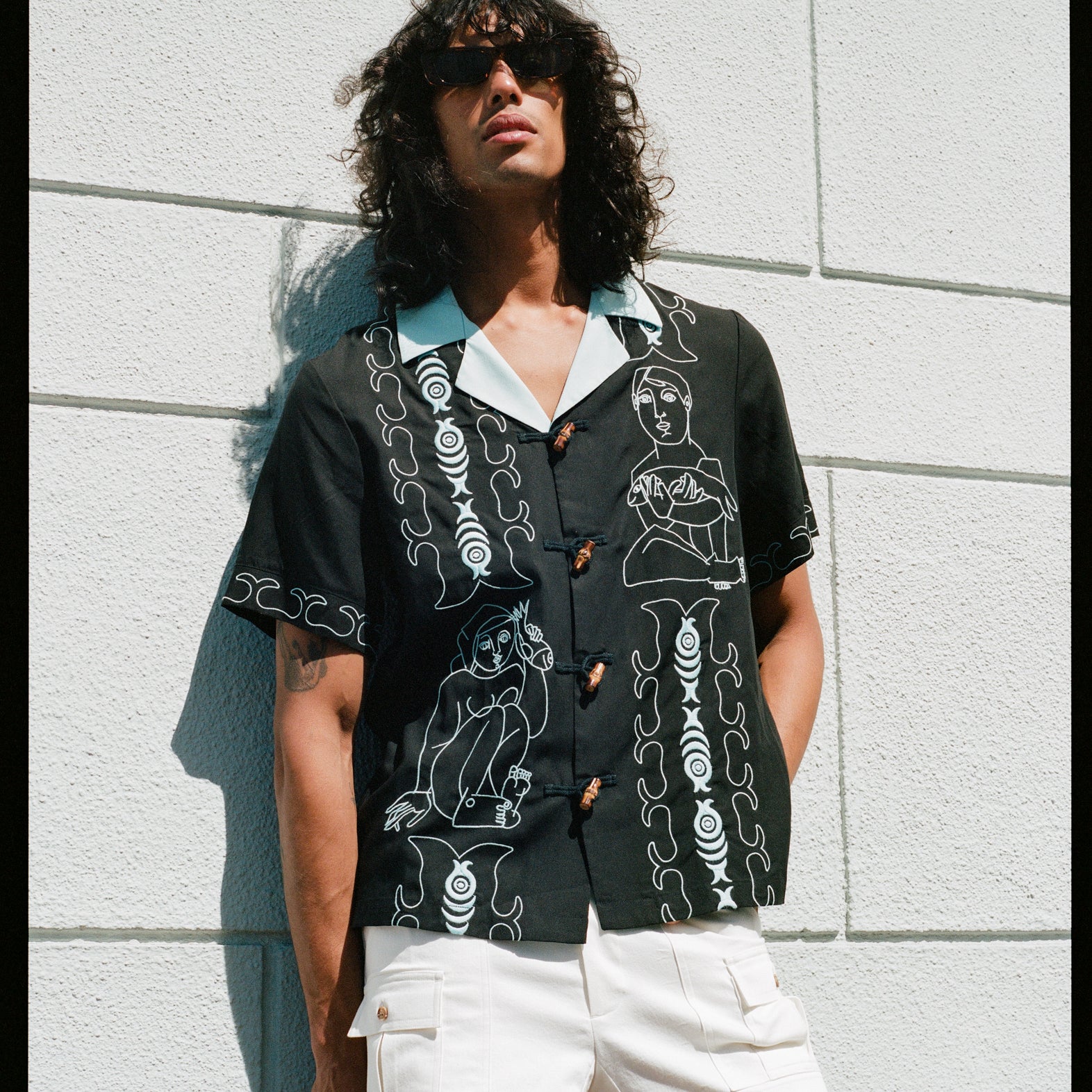 model leans against wall in sunglasses