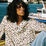 Male model wearing long sleeve with striped blue linen pants reclining on pier