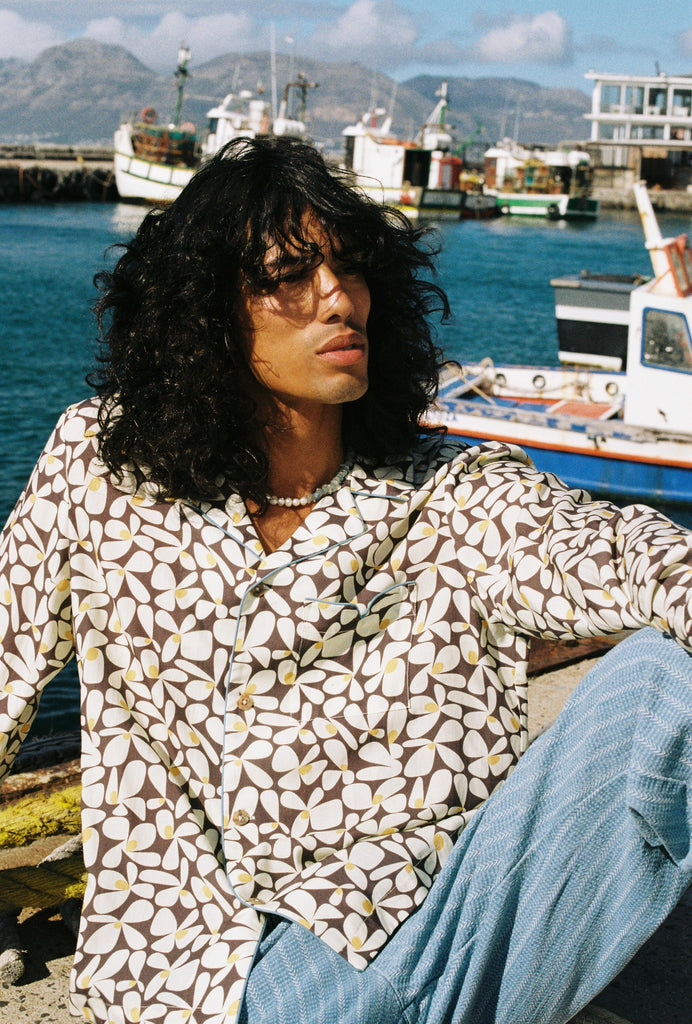 Male model wearing long sleeve with striped blue linen pants reclining on pier