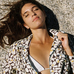 Female model laying on rock with eyes closed wearing shirt over bikini
