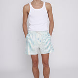 Male model with hands in pockets wearing trunks with a white tank