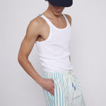 Male model wearing cap with white tank top and tombolo blue striped swim trunks