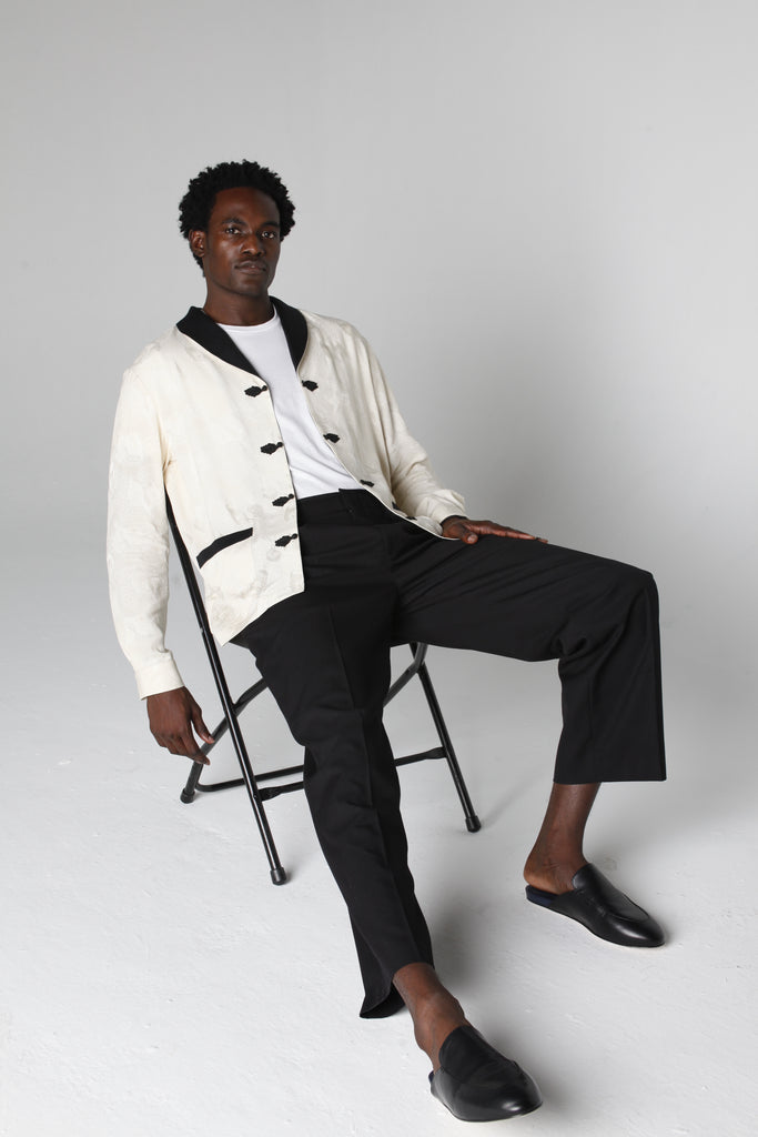 Man sits on chair in photo studio wearing unbuttoned jacket staring at camera