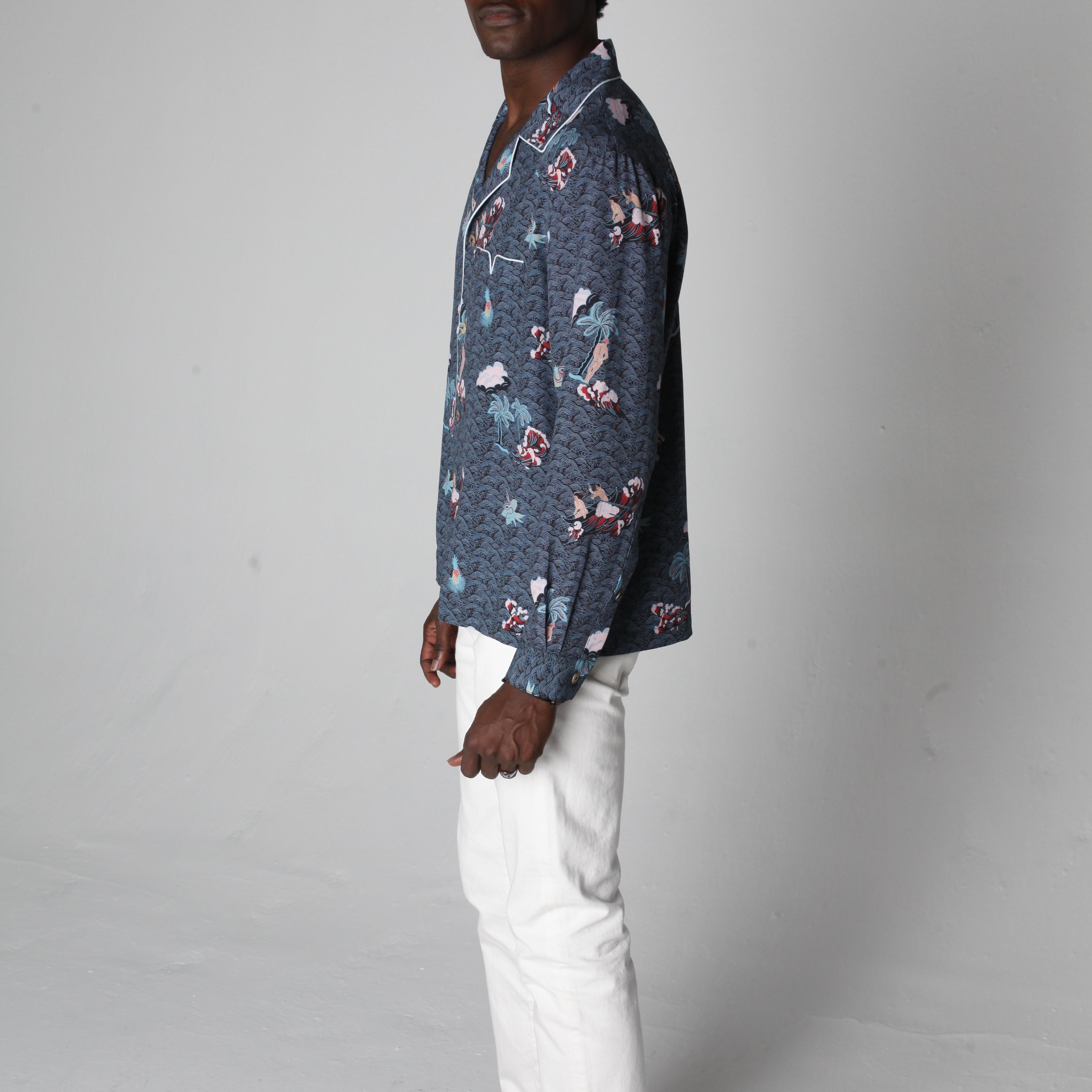 male model wearing top with white pants looking over his right shoulder in a photo studio