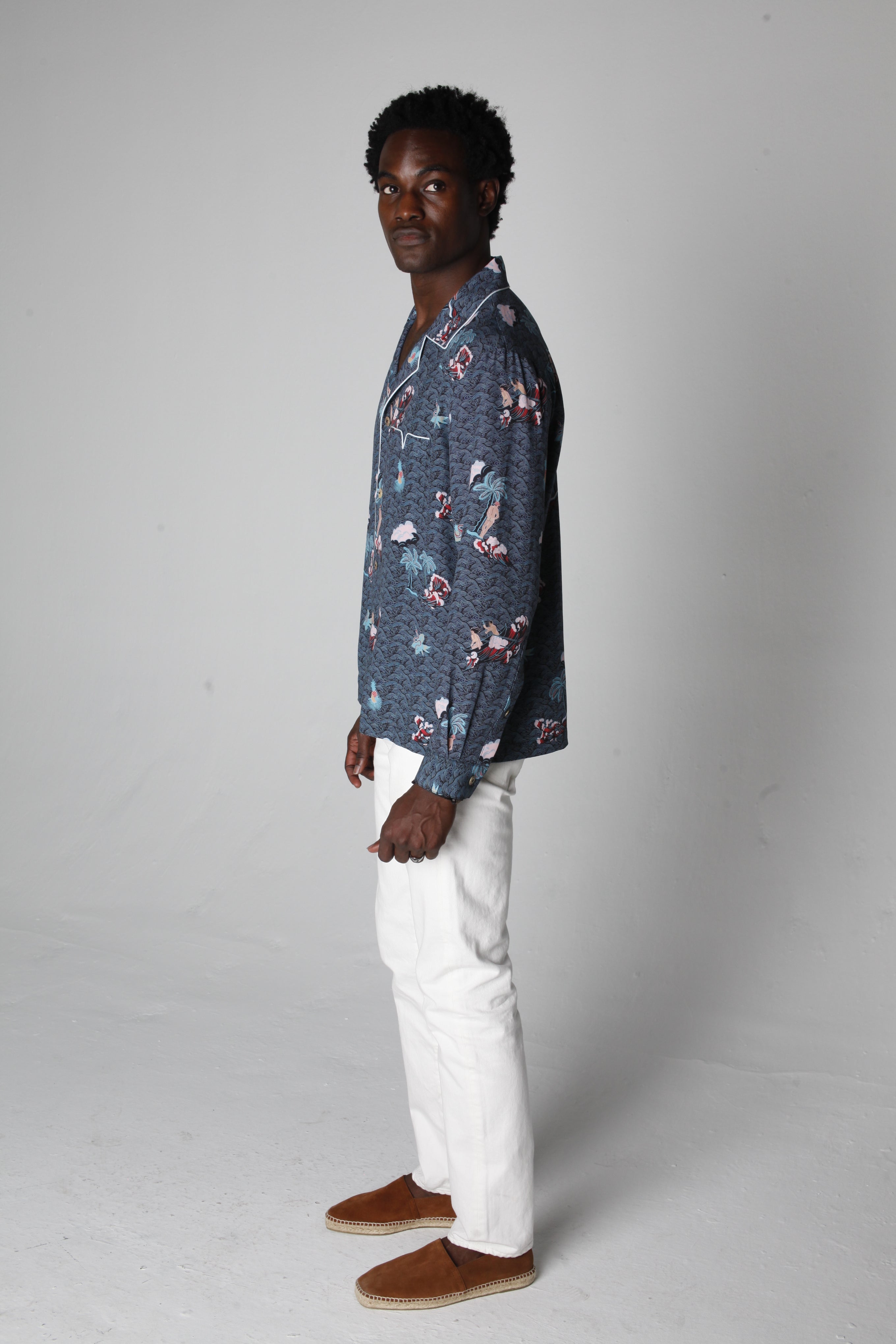 male model wearing top with white pants looking over his right shoulder in a photo studio