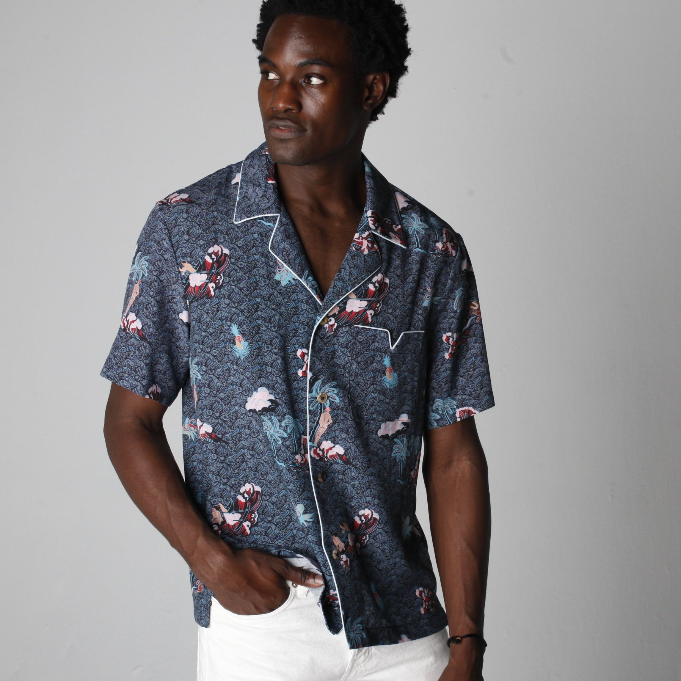 male model wearing top with white pants looking over his left shoulder in a photo studio