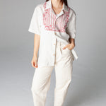 Female model wearing shirt with off white pants and red earrings