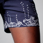 close up of mermaids riding fish embroidery along bottom hem of swim trunks